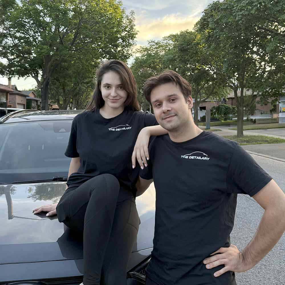 Founder and co-founder stand next to their car, smiling and looking in the camera